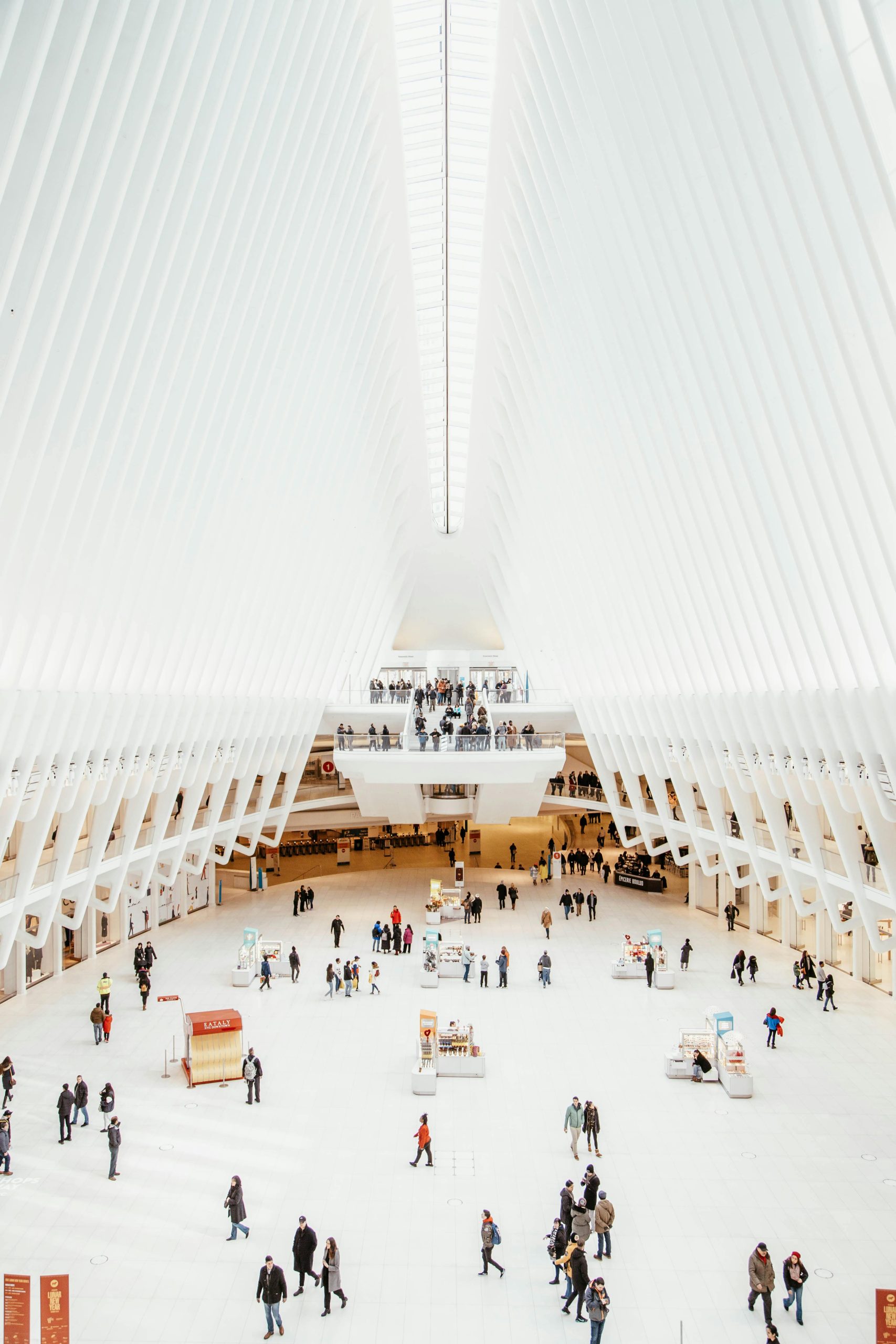 The majestic interior of the World Trade Center Oculus in NYC with people milling about, captured from above.